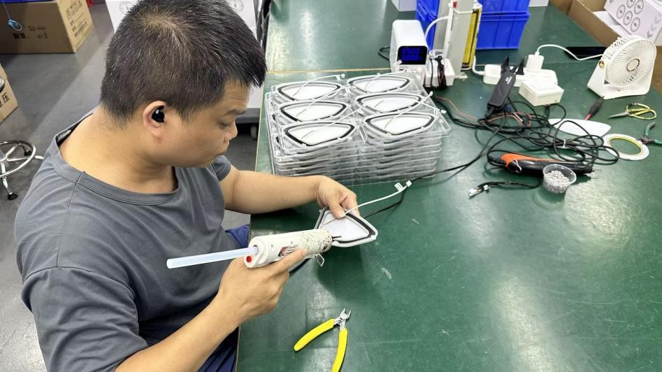 A worker using a glue gun along a speaker-cover component at a workbench