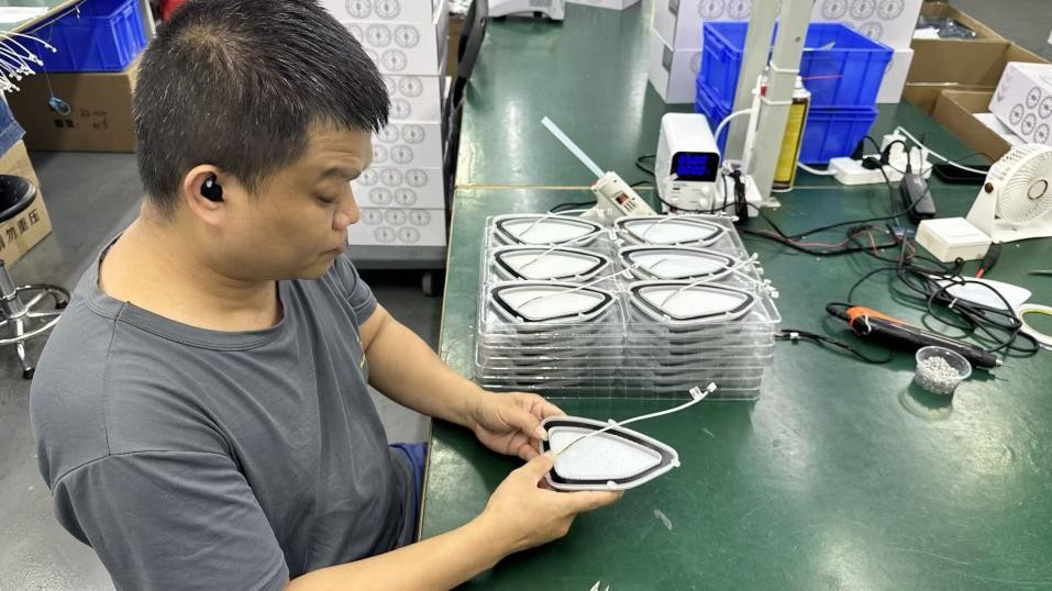 A worker positioning an illuminated speaker-cover component by hand at an assembly bench