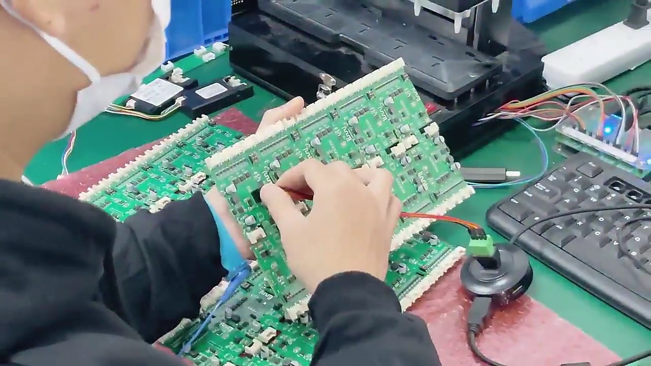 A circuit board being handled at a workbench, with a hand-held contact tool visible