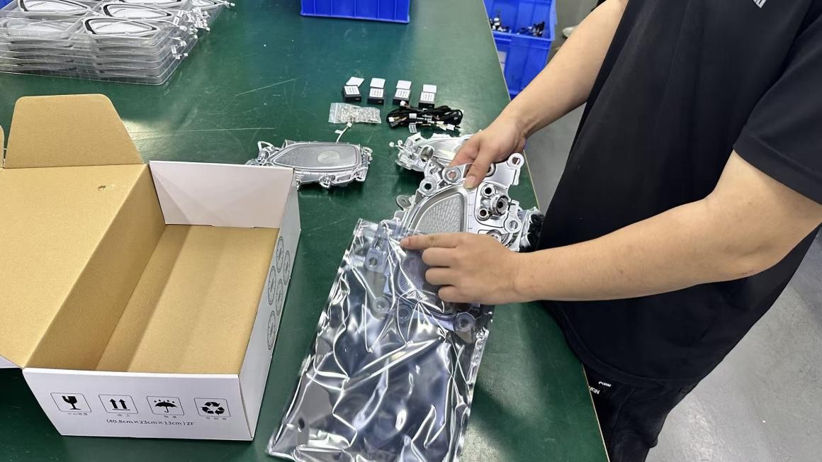 A worker placing an interior component in a protective bag beside a packing box