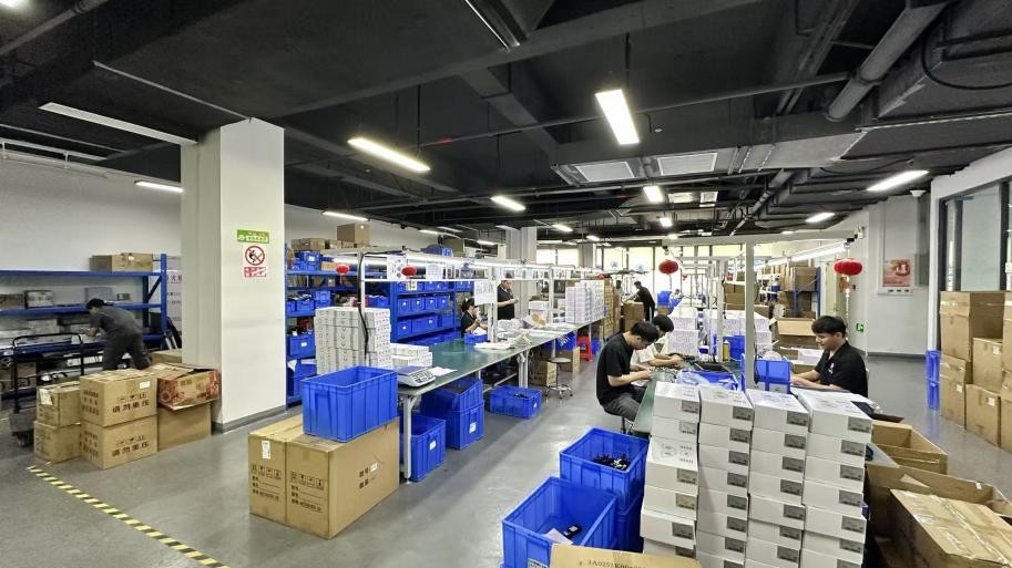 Employees at assembly benches in the CKCP workshop, with components, trays and packed boxes